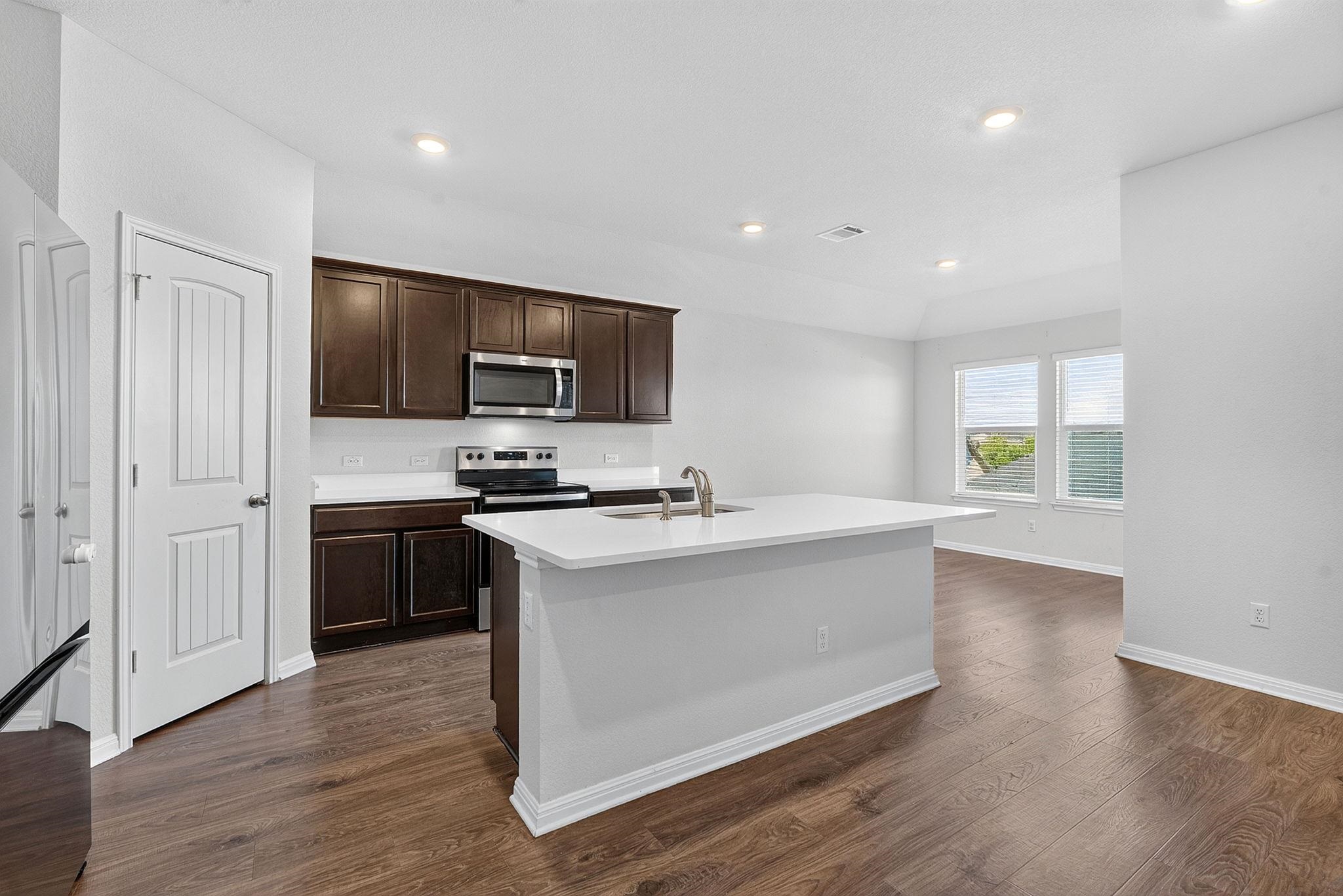 Rich wood-inspired flooring and crisp white countertops define this modern, open-concept kitchen.