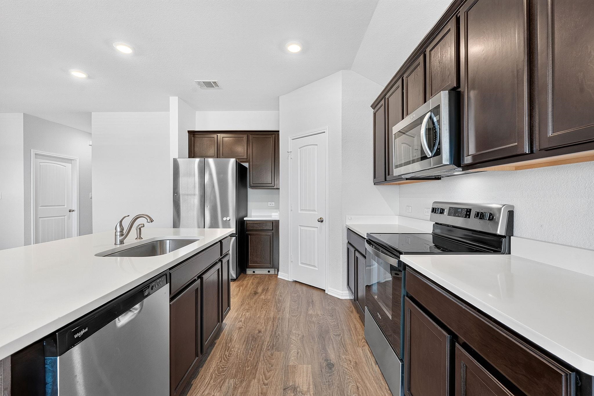 Rich dark wood cabinetry contrasts with sleek solid surface countertops and stainless appliances.