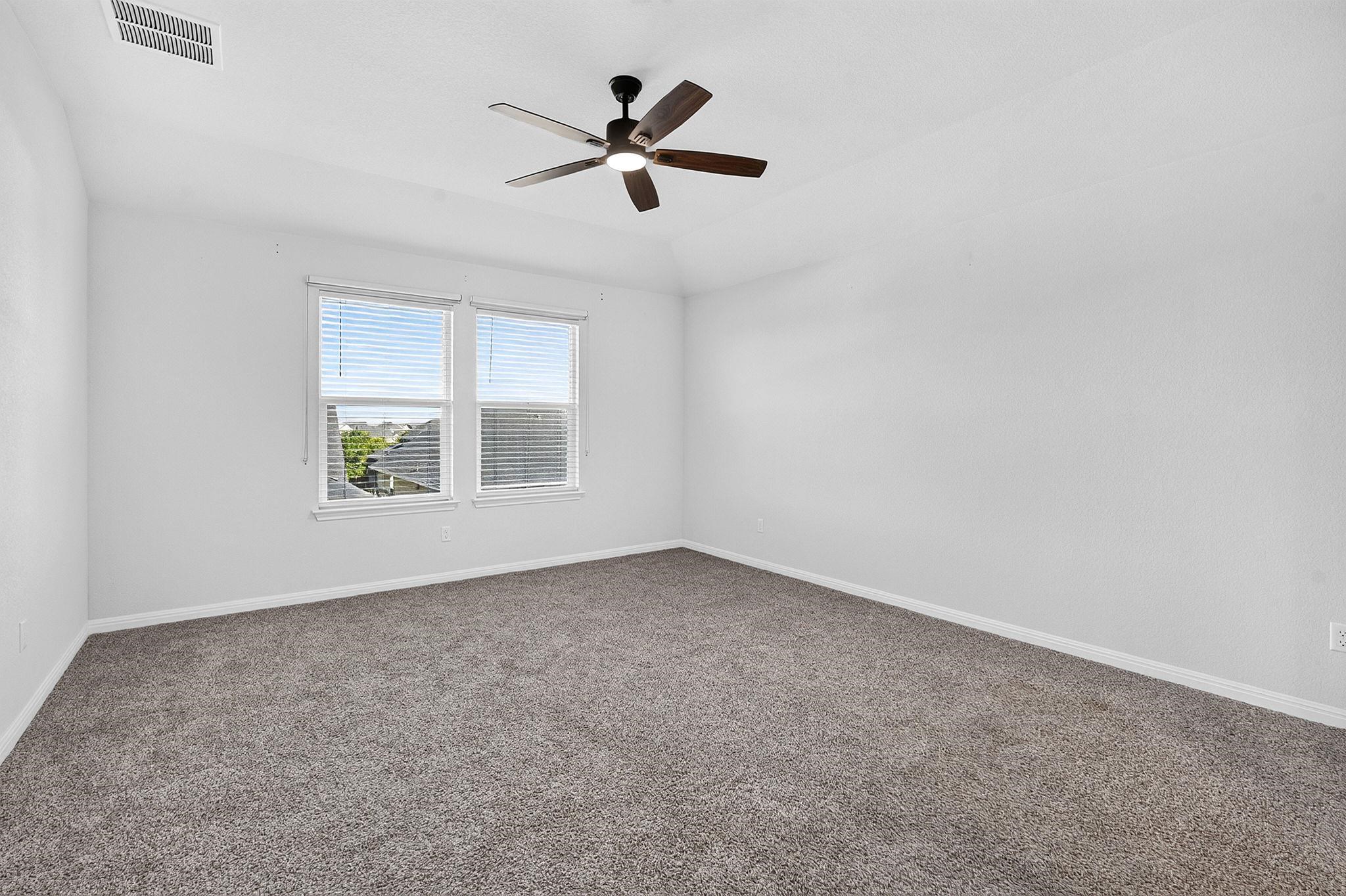 Plush carpeting anchors this spacious bedroom featuring a subtly recessed tray ceiling detail.