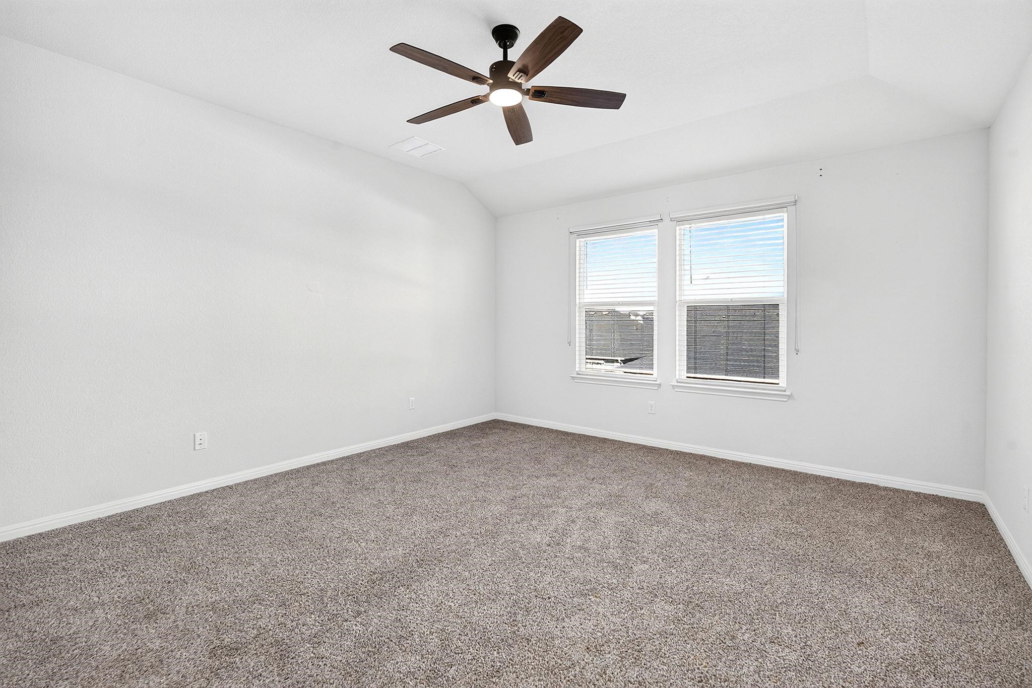 Plush carpeting anchors this bedroom under vaulted ceilings and tall windows.