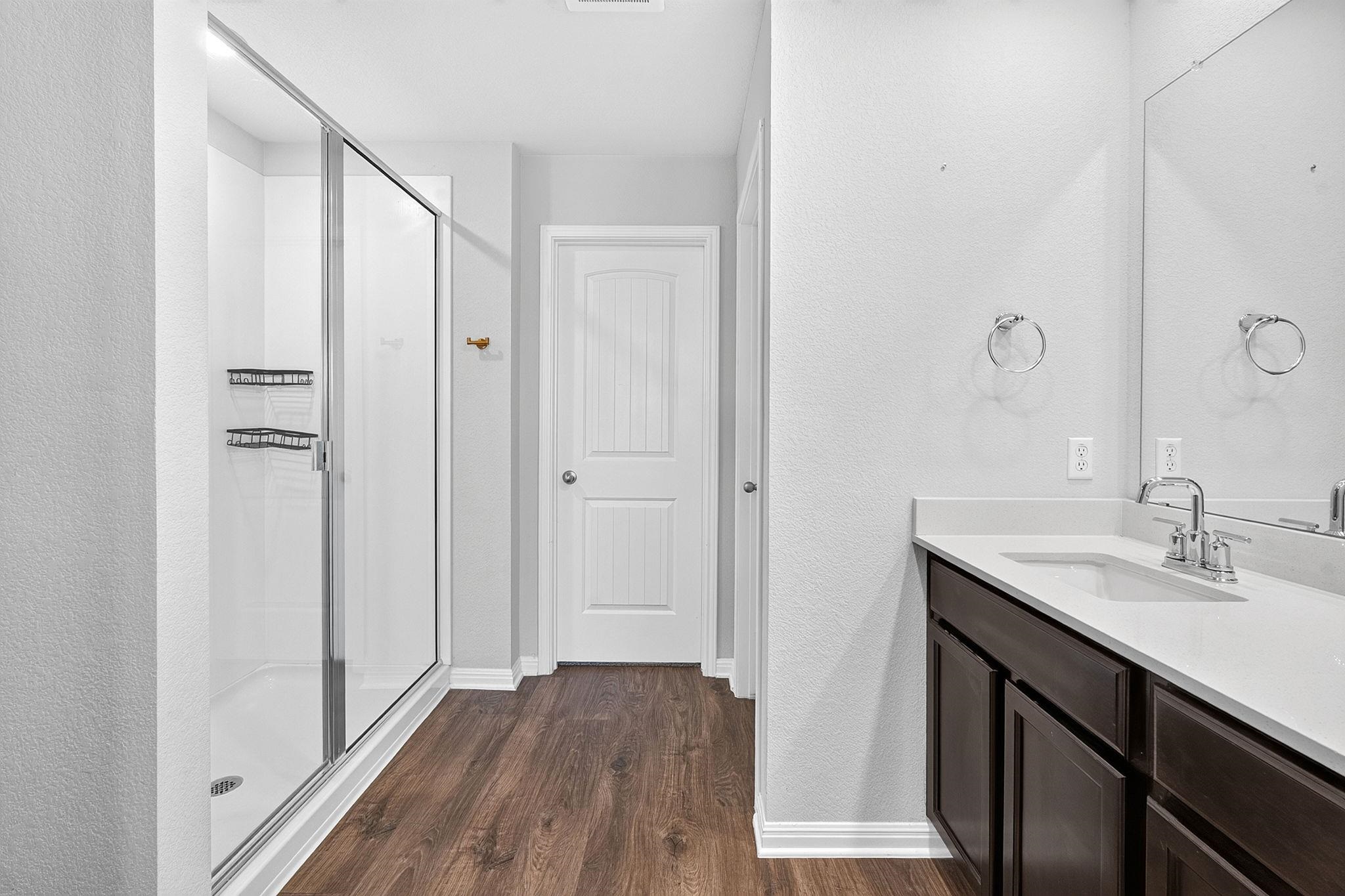 A glass-enclosed walk-in shower pairs with a dark-cabinet vanity on wood-look flooring.