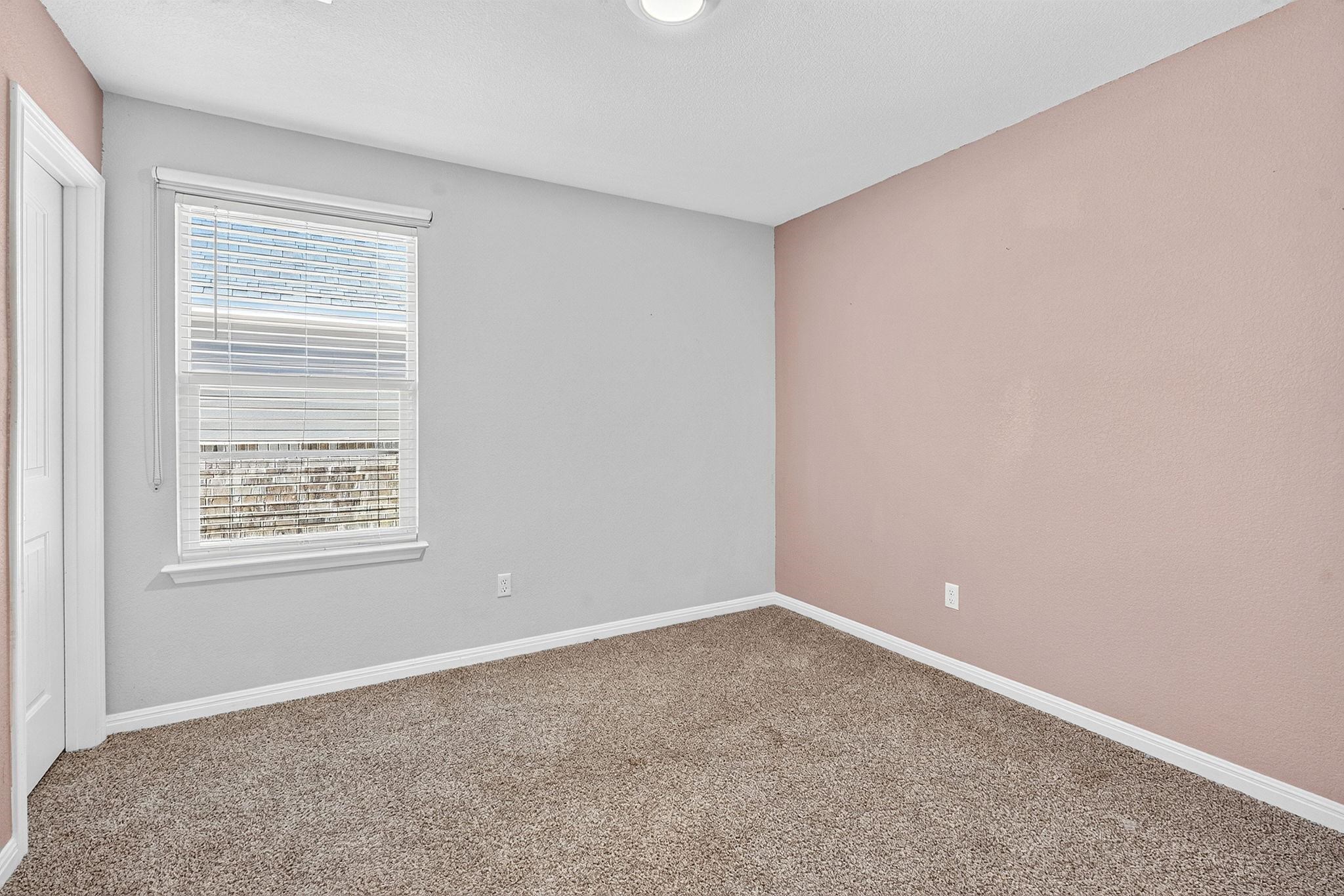 A quiet bedroom features plush carpeting and a large window providing ample natural light.