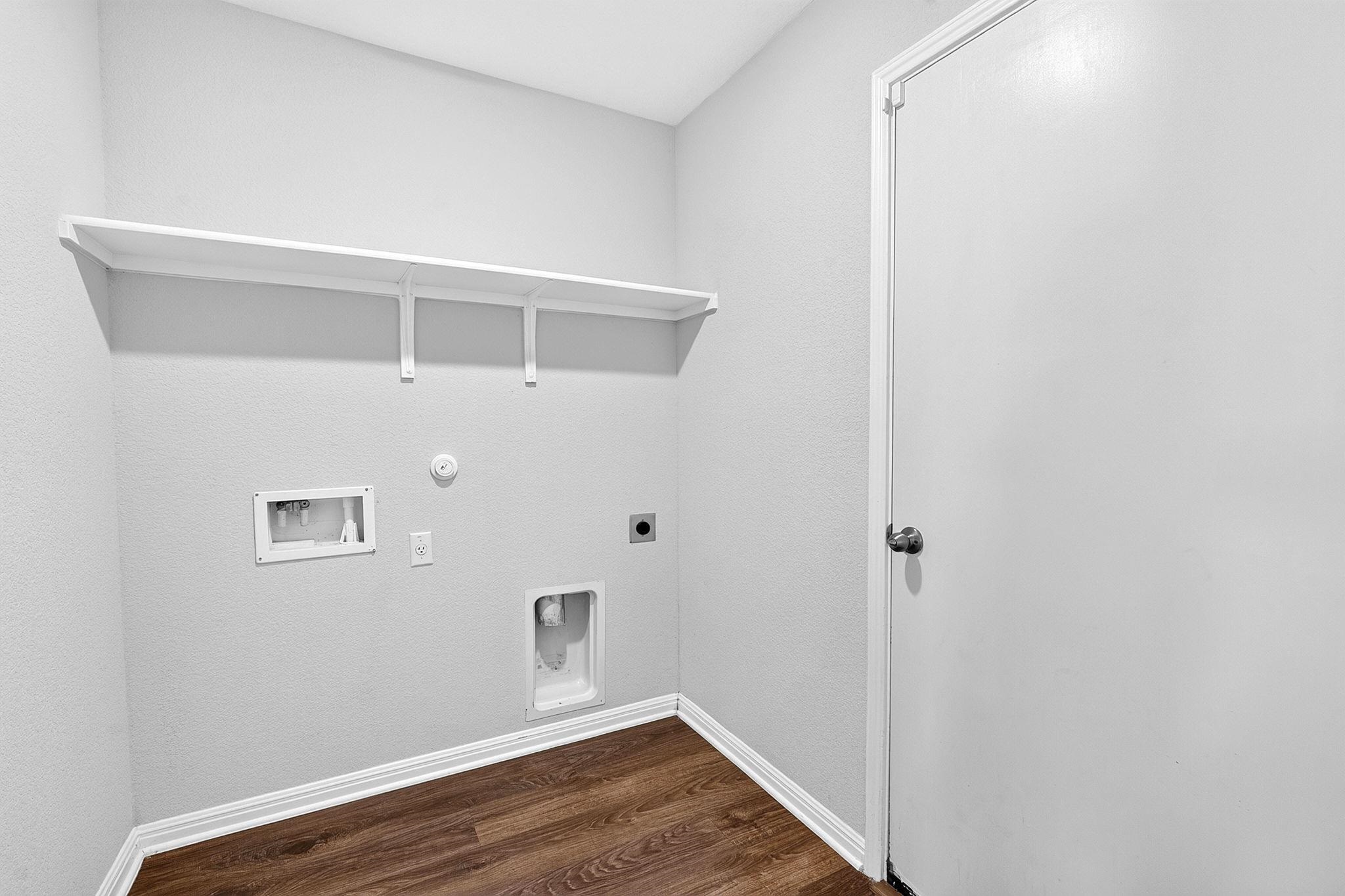 A dedicated laundry space features warm wood-look flooring and a convenient built-in storage shelf.