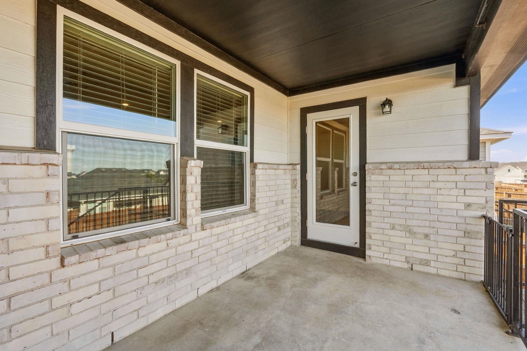 A covered balcony with concrete floors, light brick wainscoting, and a glass-paneled door.