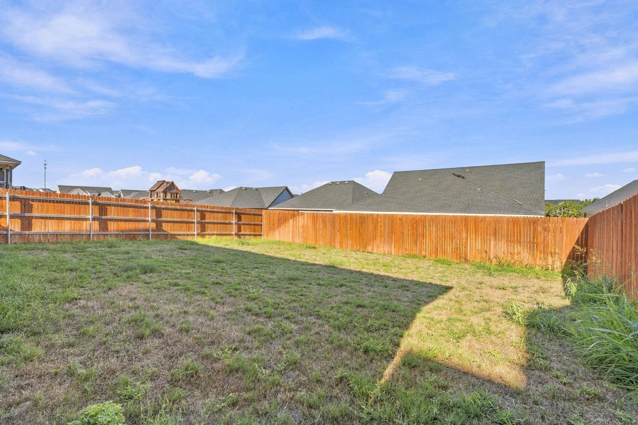 An expansive level lawn is fully enclosed by a tall wooden privacy fence.