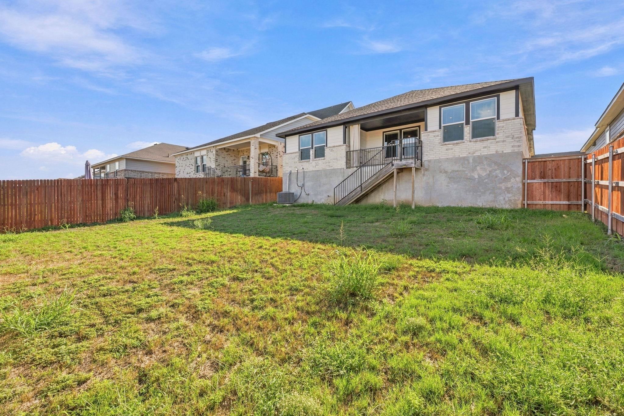 A spacious grassy lawn is fully enclosed by a sturdy wooden privacy fence.