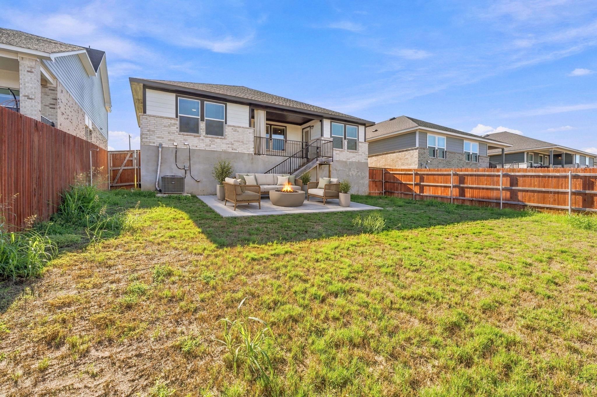 A spacious grassy lawn sits within a fully fenced backyard featuring a paved patio area.