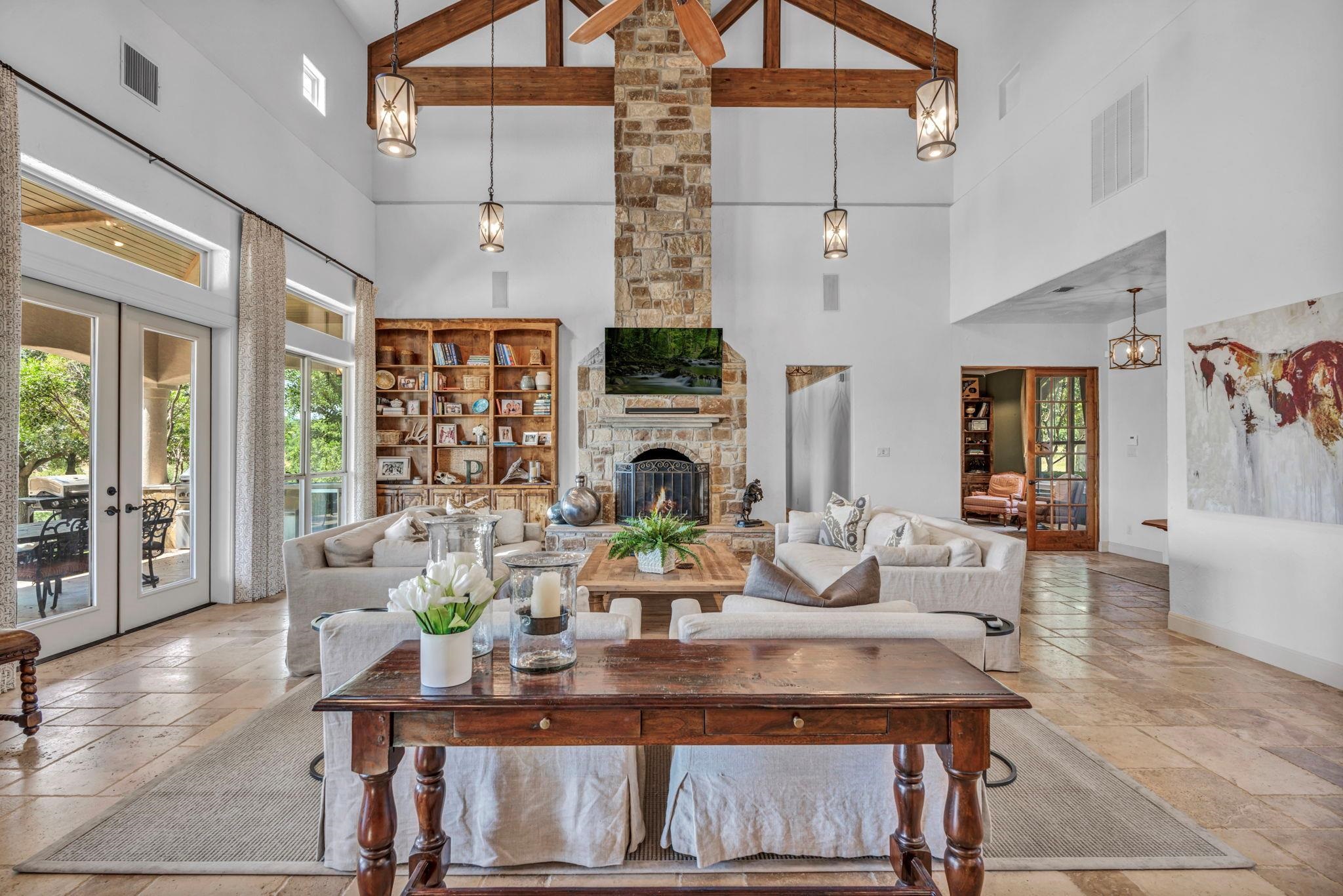 Featuring a fireplace, a ceiling fan, stone tile floors, beamed ceiling, & high vaulted ceiling
