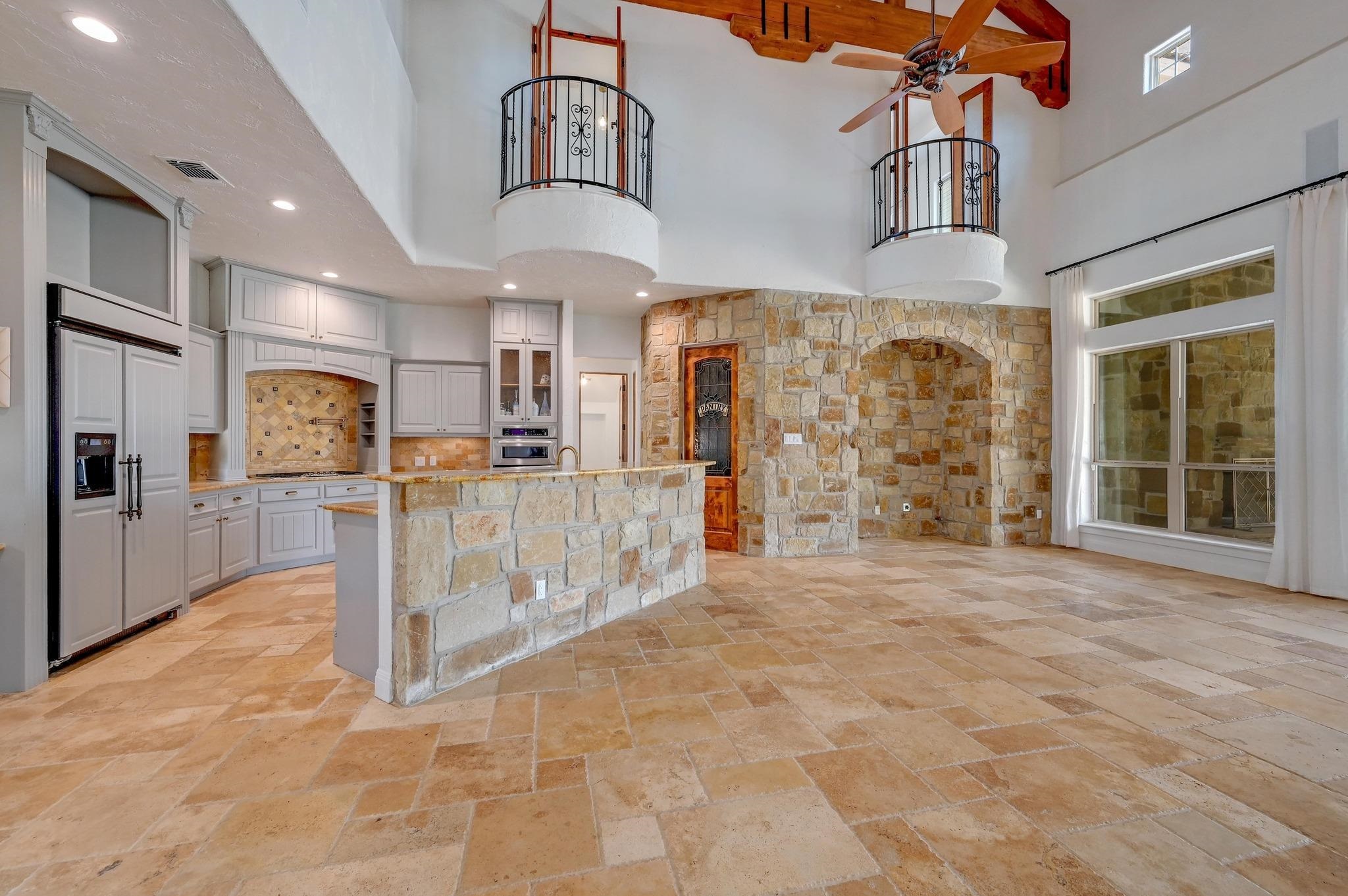 Featuring an island with sink, stone tile flooring, and hanging light fixtures, walk in pantry