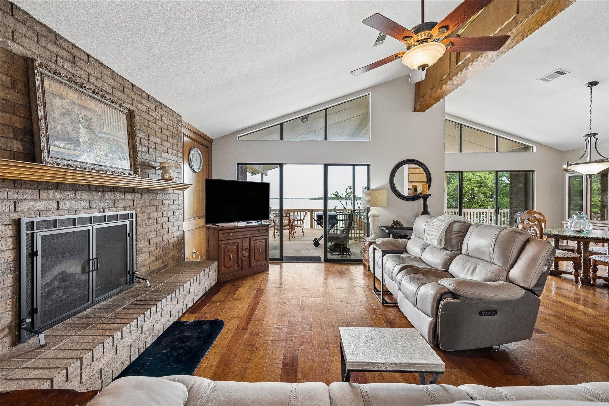 A spacious living room upstairs with vaulted ceilings and a brick fireplace opens to a scenic deck w