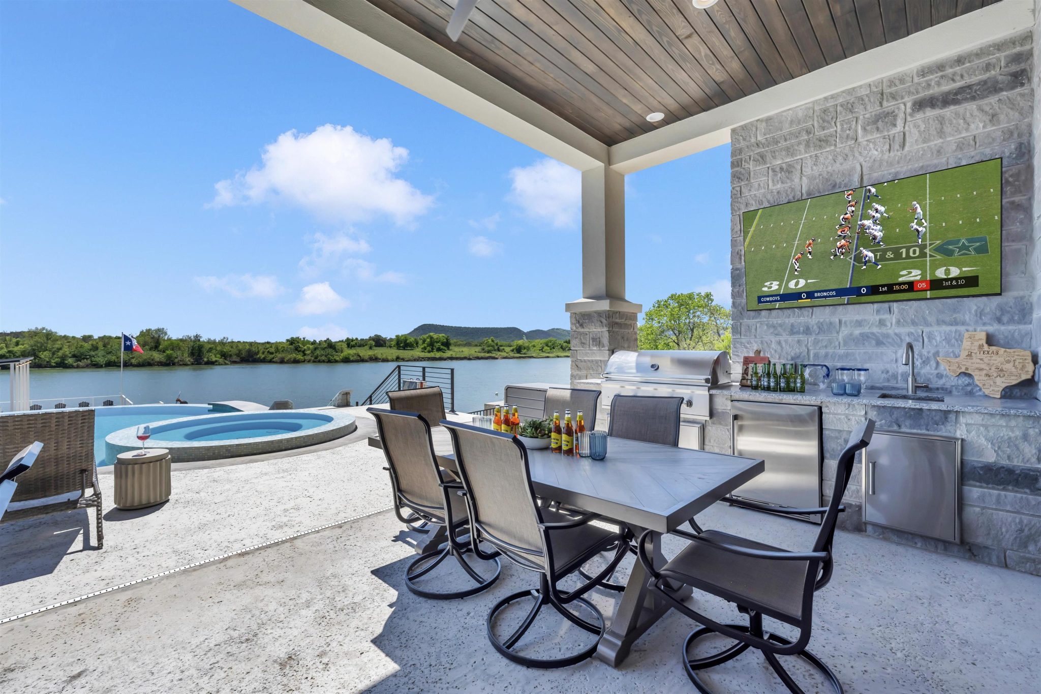 An covered stone patio overlooks the pool and serene water views.