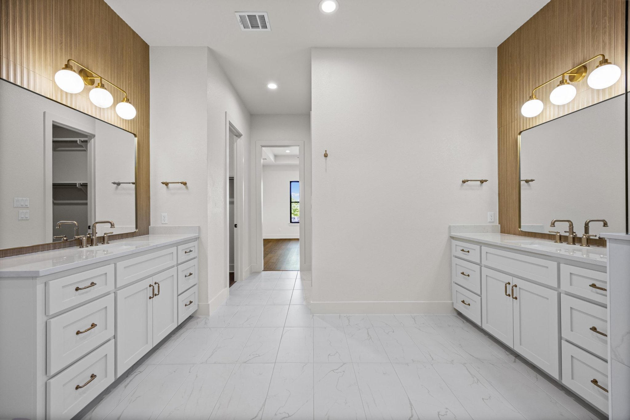 Dual vanities with sleek white cabinetry and gold hardware define the elegant primary bath space.
