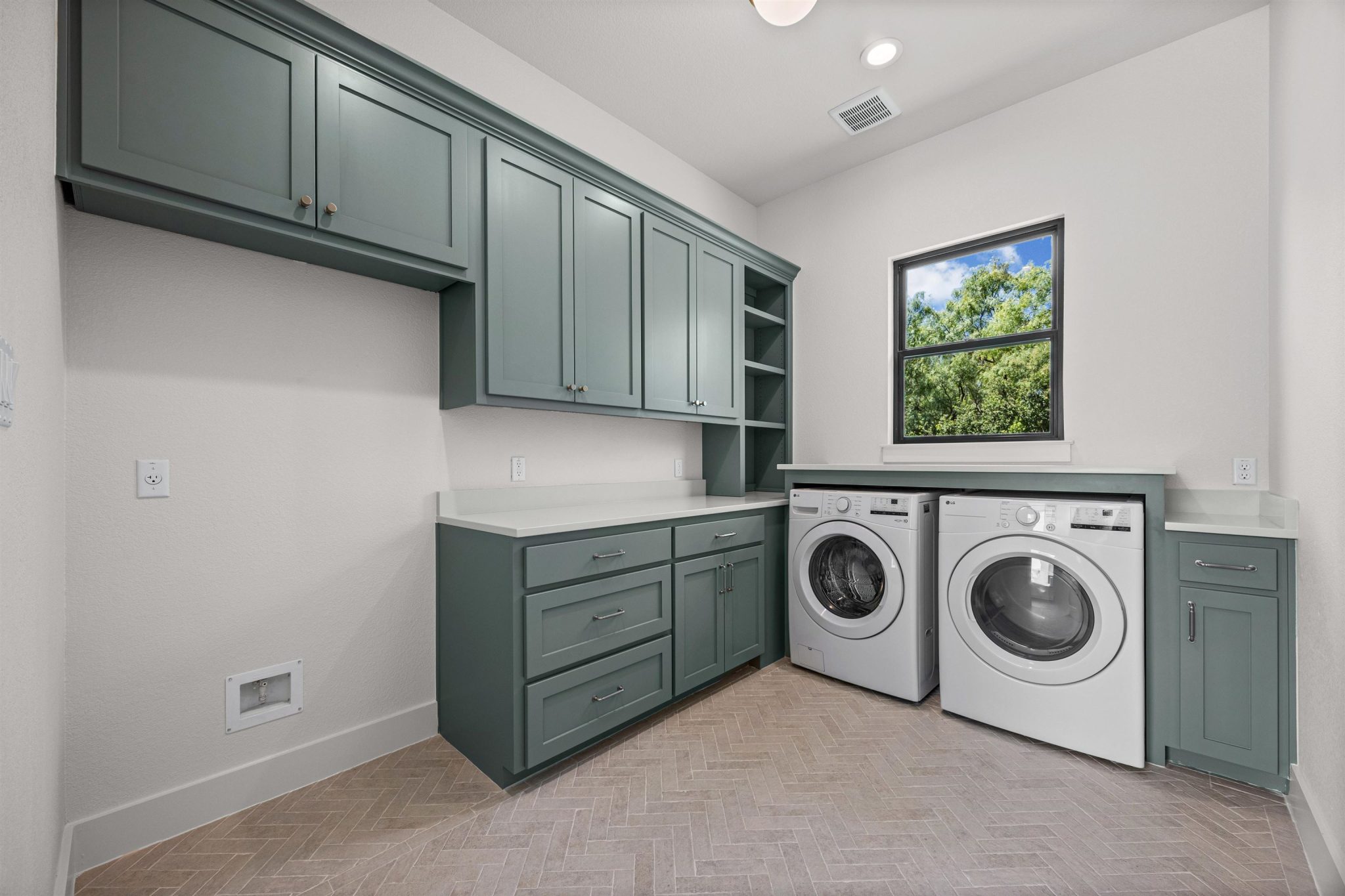 Ample cabinetry & herringbone flooring elevate this functional & naturally illuminated laundry area