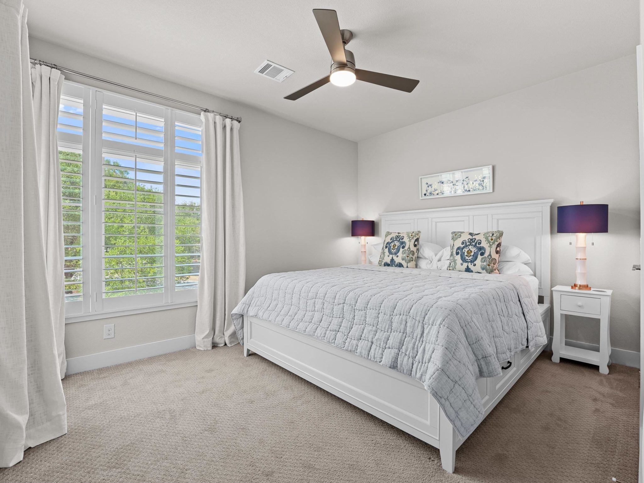 A spacious bedroom features plush carpeting and a large window looking out to leafy trees.