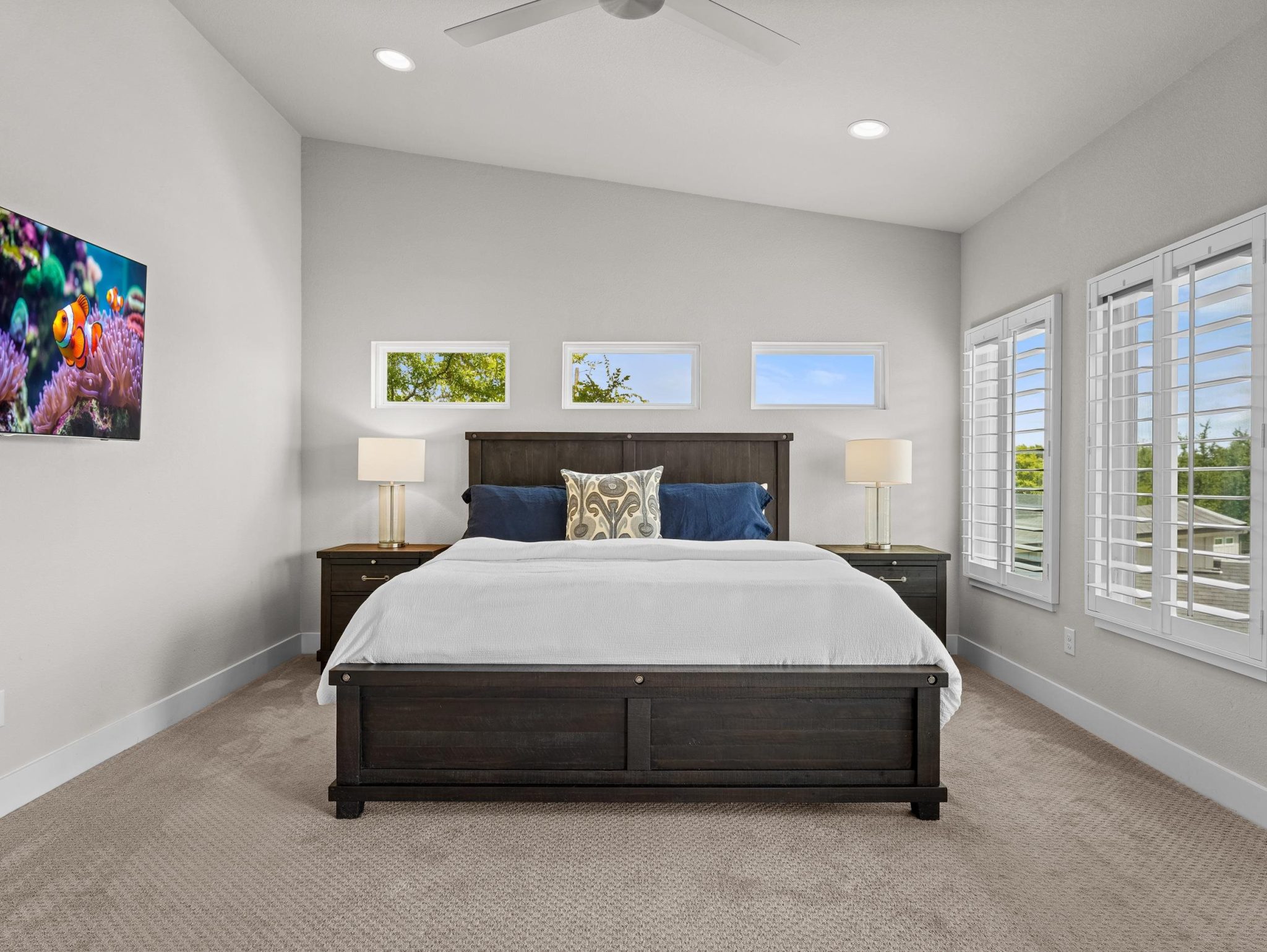 High ceilings and plantation shutters accent this serene bedroom space with plush carpeting.